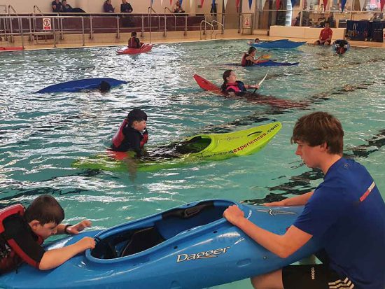 A kayaking training session taking place with the coach helping a child get into a kayak